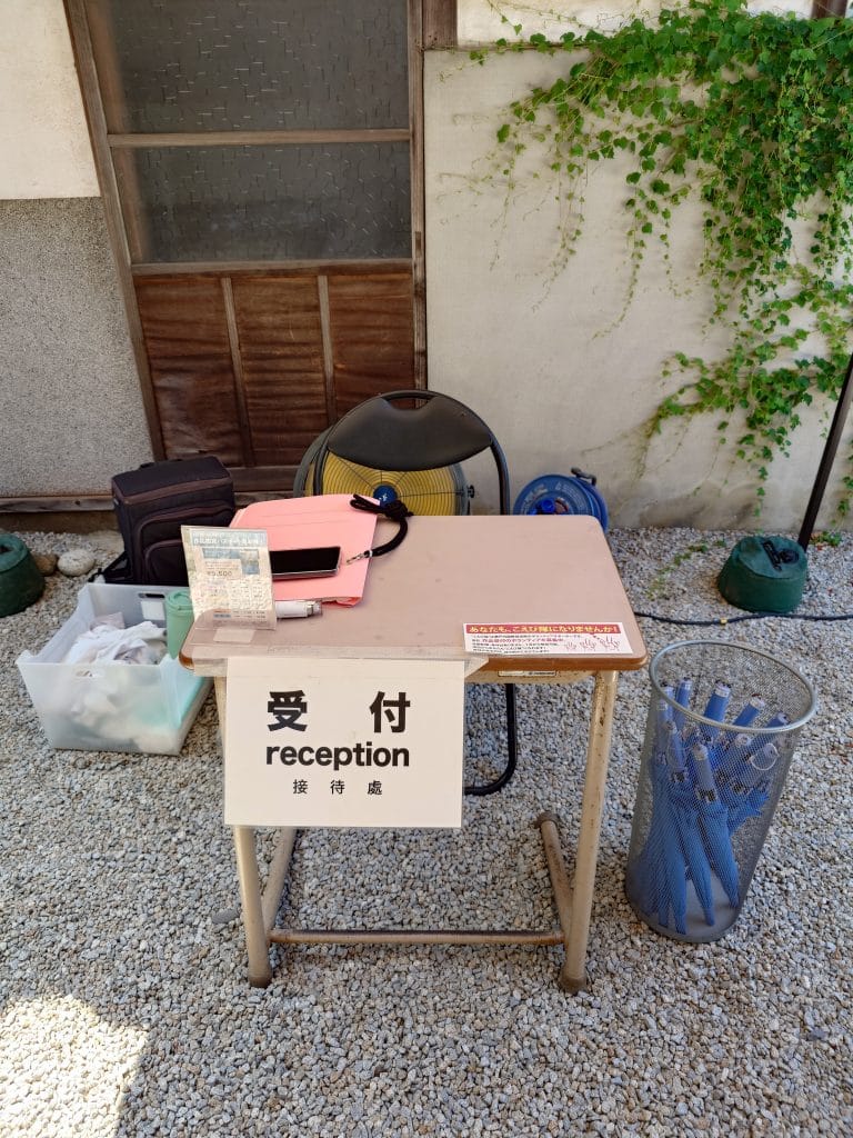 「部屋の中の部屋」的接待處，椅子後面是工業扇，旁邊的箱子裡有降溫噴霧、防蟲噴霧等用品，桌子旁籃子裡的雨傘供旅客使用