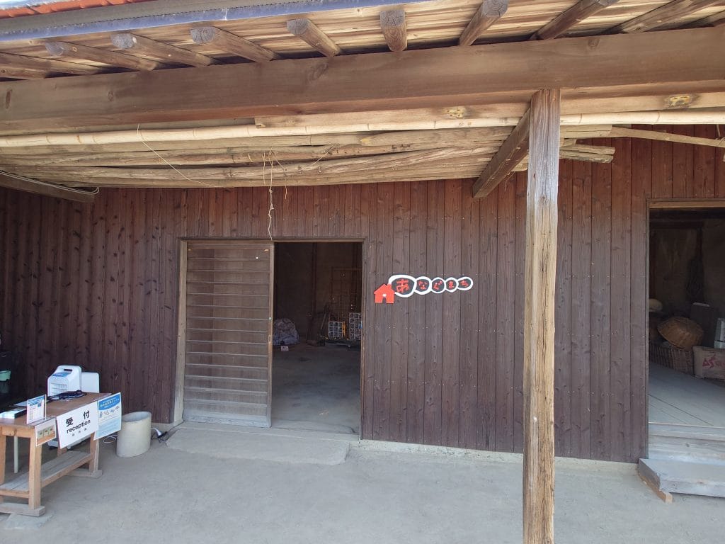 「女木島人口増加大計画 ～あなぐまち入居者募集中～」的入口與接待處，拍攝位置的後方道路上充滿沙土，當大風吹起時，很容易把沙土吹往接待處，另外，這裡有蚊蟲的滋擾，需要多加使用防蟲噴霧