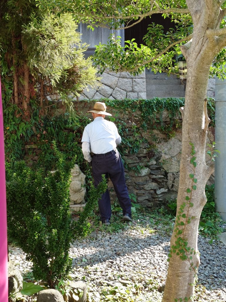 在「あなたの最初の色（私の頭の中の解―私の胃の中の溶液）」作品的搭檔的老先生，老先生空閒時，在附近進行環境清潔的背影